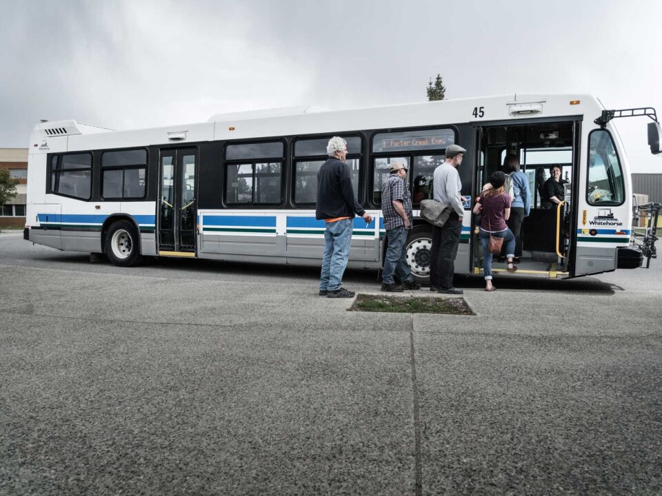 People lining up to board a City of Whitehorse bus.
