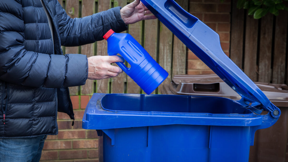 Person placing recyclable container into a large recycling bin.
